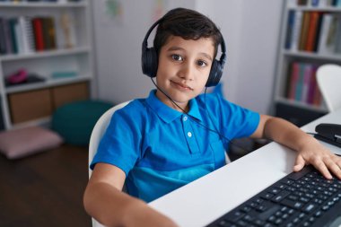 Okulda bilgisayar kullanan küçük İspanyol çocuk pozitif ve mutlu görünüyor ve kendine güvenen bir gülümsemeyle dişlerini gösteriyor. 