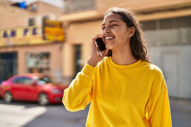 Genç Afrikalı Amerikalı kadın gülümsüyor. Kendine güveni tam. Sokakta akıllı telefondan konuşuyor.