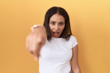 Sarı arka plan üzerine sıradan beyaz tişört giyen genç Arap kadın kameraya kızgın ve sinirli olduğunu gösteriyor. 