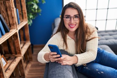 Evdeki kanepede oturan akıllı telefon kullanan genç, güzel İspanyol kadın.