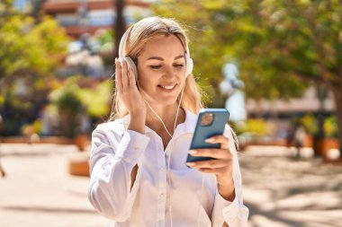Young blonde woman listening to music at park