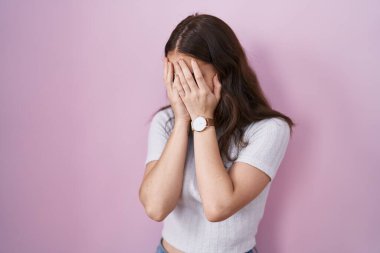 Pembe arka planda duran genç İspanyol kız. Ağlarken suratını ellerle kapatan üzgün bir ifade. depresyon kavramı. 