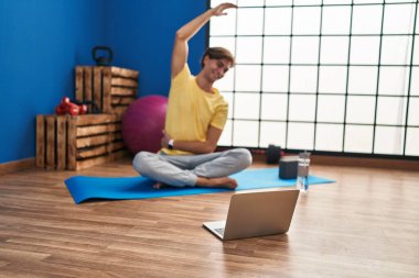 Young caucasian man smiling confident having online stretching class at sport center