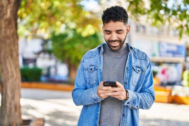 Parkta akıllı telefon kullanarak gülümseyen İspanyol genç adam.
