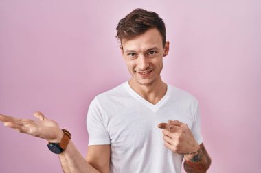 Pembe arka planda duran beyaz adam kameraya hayret ediyor ve gülümsüyor.. 