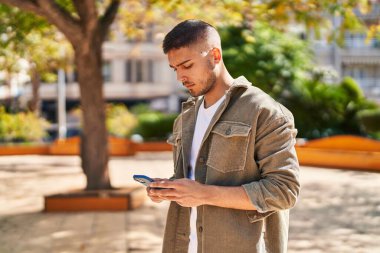 Young hispanic man using smartphone at park