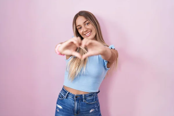 Young Blonde Woman Standing Pink Background Smiling Love Doing Heart — Stock fotografie