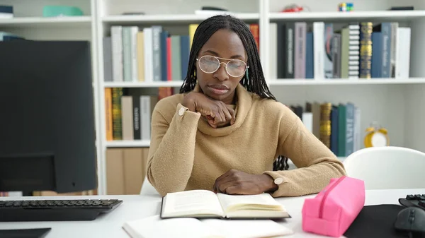 African woman reading a book sitting on desk at library university