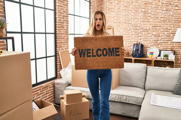 Young Blonde Woman Holding Welcome Doormat New Home Shock Face — Stock Photo, Image