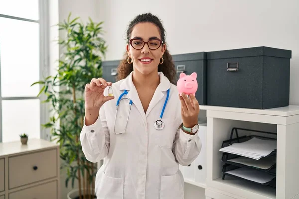 stock image Young hispanic woman holding vaccine and piggy bank winking looking at the camera with sexy expression, cheerful and happy face. 