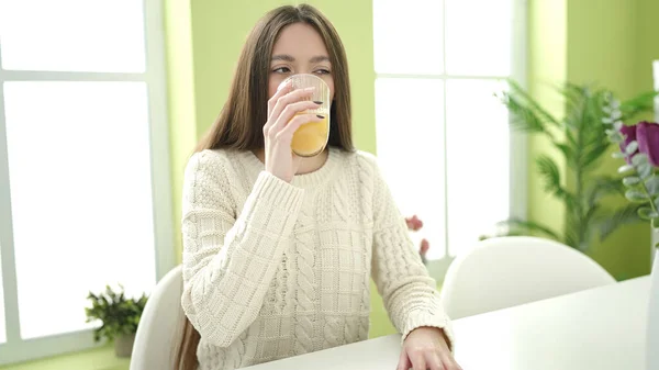 若いです美しいですヒスパニック女性飲むガラスのオレンジジュースのテーブルの上に家に座って — ストック写真
