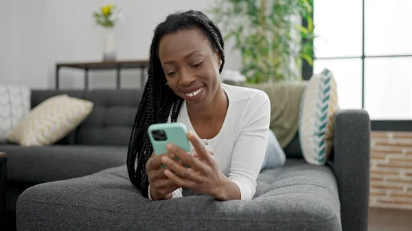 African American Woman Using Smartphone Lying Sofa Home — стоковое фото