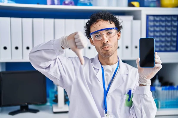 在科学家实验室工作的西班牙裔男性 他们用愤怒的面孔展示智能手机屏幕 负面信号显示他们不喜欢戴大拇指 拒绝的概念 — 图库照片
