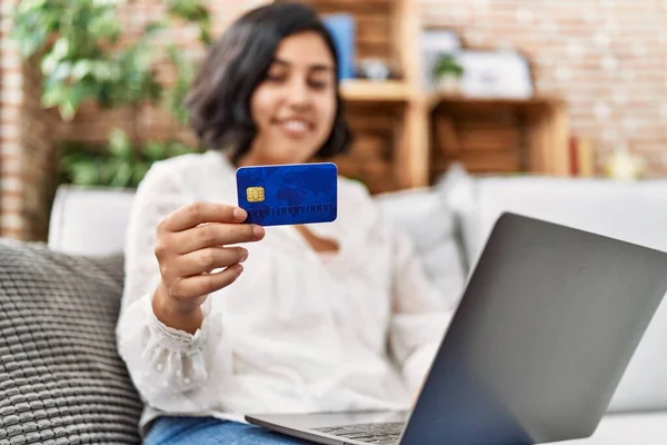 年轻的拉丁女人坐在家里的沙发上 用笔记本电脑和信用卡 — 图库照片