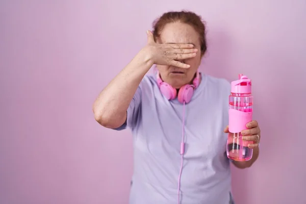 Starší Žena Sportovním Oblečení Sluchátkách Zakrývající Oči Rukou Vypadá Vážně — Stock fotografie