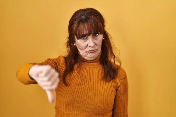 黄色の背景に立っている中年のパニック女性は 親指を下にジェスチャーで拒絶と否定を示す不満と怒りを見ています 悪い表現 — ストック写真