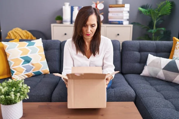 Middle age brunette woman opening cardboard box skeptic and nervous, frowning upset because of problem. negative person.