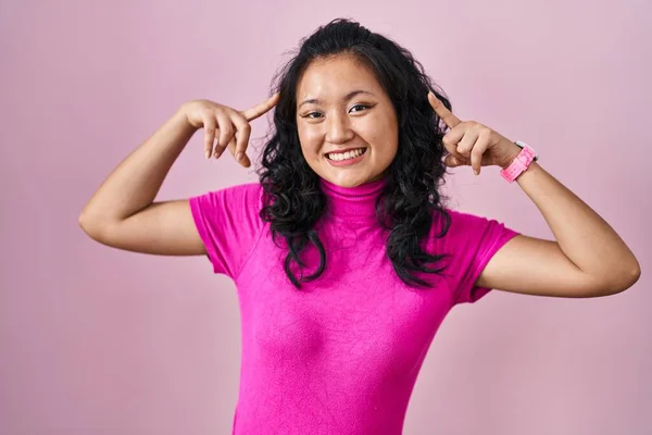 Jonge Aziatische Vrouw Staan Roze Achtergrond Glimlachen Wijzend Naar Hoofd — Stockfoto