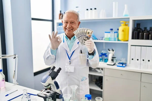 研究室で働いている灰色の髪を持つ上級科学者は 指でOkサインを行うドルを保持します 笑顔優しいジェスチャー優れたシンボル — ストック写真