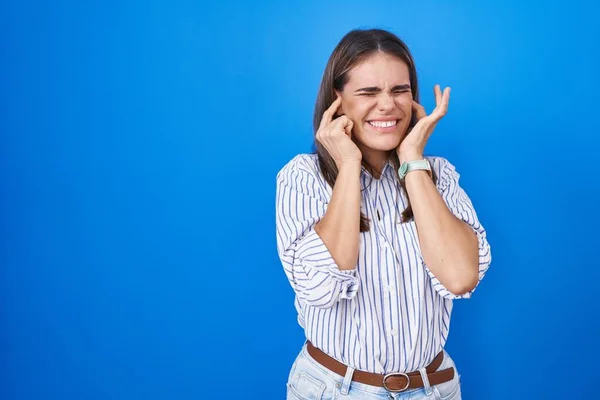 西班牙裔年轻女子站在蓝色背景之上 用手指捂住耳朵 对嘈杂的音乐感到恼怒 聋人概念 — 图库照片