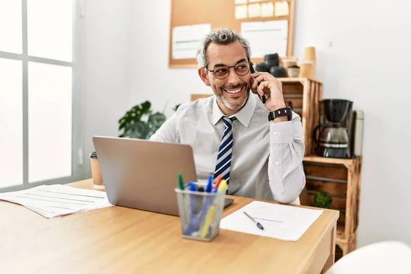 オフィスでスマートフォンで話すノートパソコンを使用している中年の白髪のビジネスマン — ストック写真