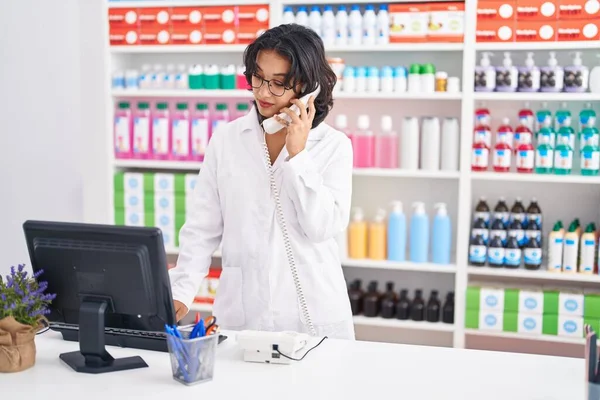 Young Beautiful Hispanic Woman Pharmacist Talking Telephone Using Computer Pharmacy — Zdjęcie stockowe