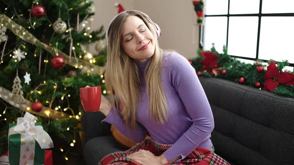 Genç Sarışın Müzik Dinleyen Kahve Içen Noel Ağacının Yanında Oturan — Stok fotoğraf