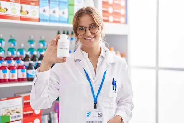 Young Blonde Girl Pharmacist Smiling Confident Holding Pills Bottle Pharmacy — Foto Stock