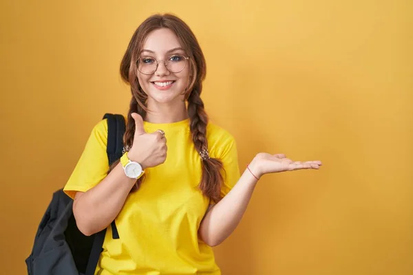 Mladá Běloška Sobě Studentský Batoh Přes Žluté Pozadí Ukazuje Dlaň — Stock fotografie
