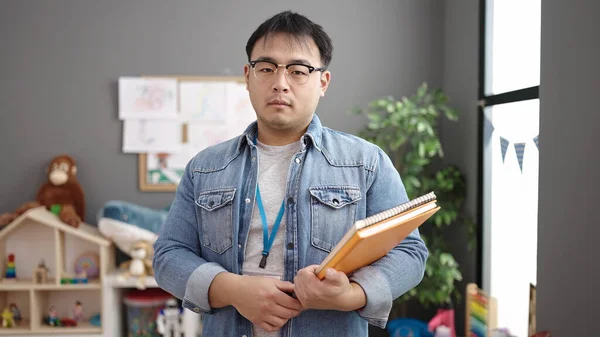 Młody Chiński Człowiek Nauczyciel Trzymając Książki Relaksującą Ekspresją Przedszkolu — Zdjęcie stockowe