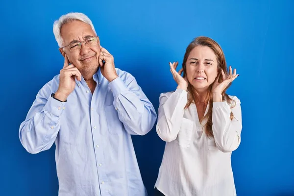 中世のパニックカップルは 大きな音楽のノイズのためにいらいらする表現で指で耳を覆う青い背景の上に立っています 聴覚障害の概念 — ストック写真