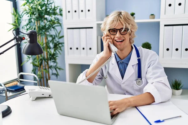 Young Blond Man Doctor Using Laptop Talking Telephone Clinic — Stock Photo, Image