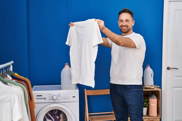 Junger Kaukasier Lächelt Selbstbewusst Und Hält Sauberes Shirt Der Waschküche — Stockfoto