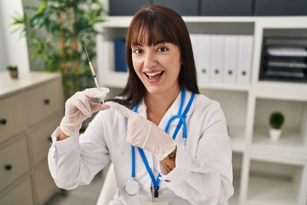 Młoda Brunetka Lekarz Kobieta Trzyma Strzykawkę Uśmiechnięty Szczęśliwy Wskazując Ręką — Zdjęcie stockowe