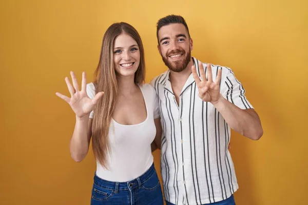 年轻夫妇站在黄色的背景上 用9号手指指指指点点 面带微笑 自信而快乐 — 图库照片