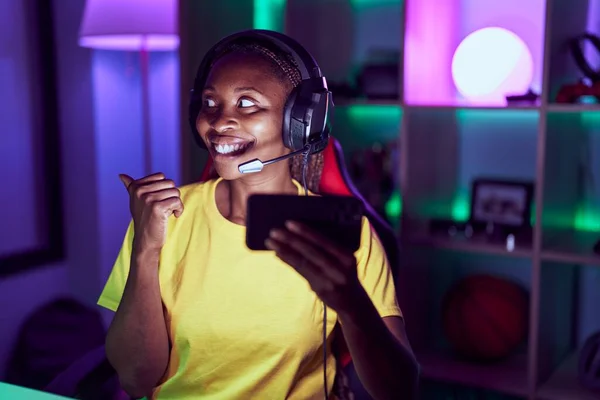 アフリカ系アメリカ人女性ゲームをプレイしていますスマートフォンを指差す親指で側に笑顔幸せなオープン口 — ストック写真