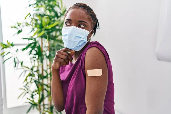 stock image Beautiful black woman getting vaccine showing arm with band aid serious face thinking about question with hand on chin, thoughtful about confusing idea 