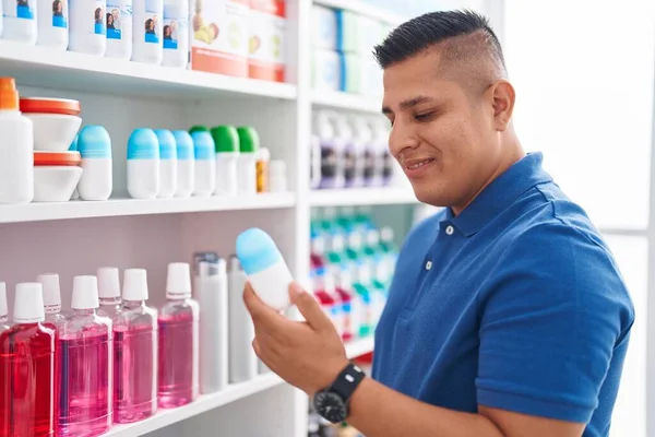 Young latin man customer smiling confident holding deodorant at pharmacy