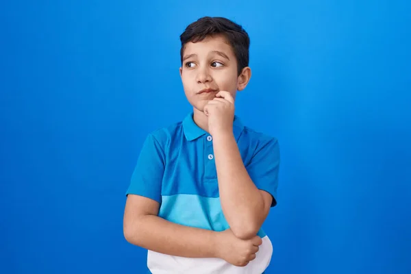 Liten Latinamerikansk Pojke Står Över Blå Bakgrund Tänkande Koncentrerad Tvivel — Stockfoto