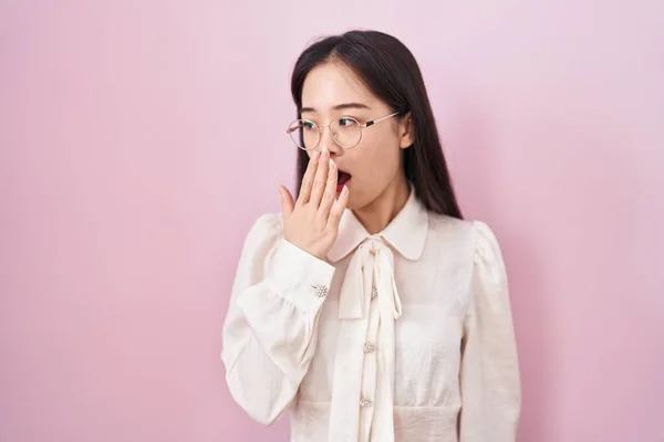 站在粉色背景上的年轻中国女人厌烦了打呵欠 疲倦得用手捂住嘴 烦躁不安和困倦 — 图库照片