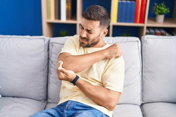 Young Hispanic Man Sitting Sofa Suffering Elbow Pain Home — Fotografie, imagine de stoc