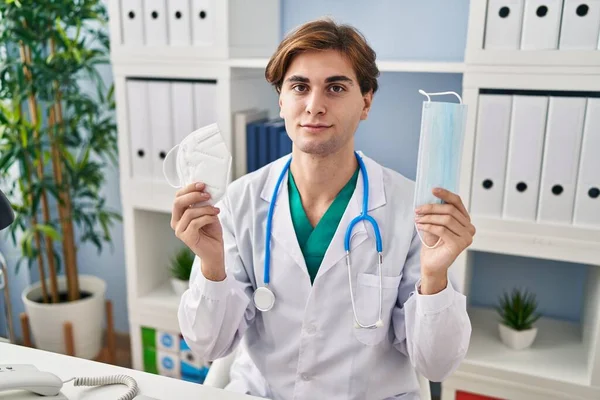 Young Doctor Man Holding Two Safety Mask Relaxed Serious Expression — Stock Photo, Image