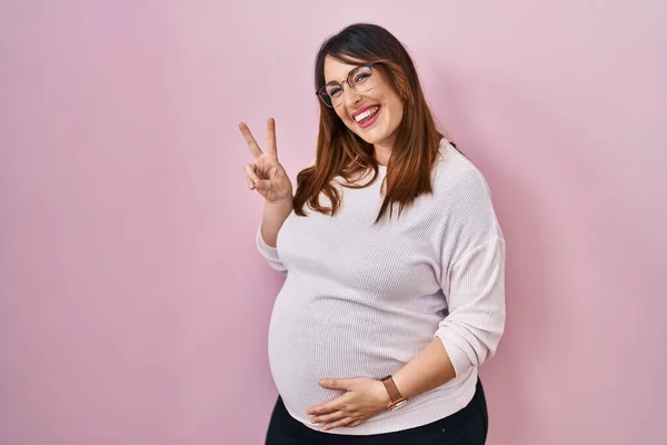 Těhotná Žena Stojící Nad Růžovým Pozadím Ukazující Ukazující Prsty Číslo — Stock fotografie
