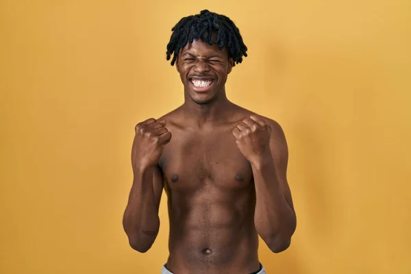 腕を上げ 目を閉じて勝利の笑顔を祝うために興奮して恥知らずに立っているドレッドロックを持つ若いアフリカの男 勝者のコンセプト — ストック写真