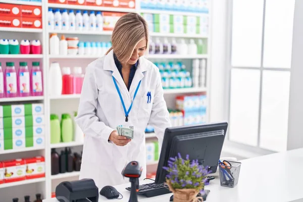 Young Blonde Woman Pharmacist Using Computer Holding Dollars Pharmacy — Stockfoto