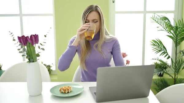 若いですブロンド女性持っています朝食使用ノートパソコンにホーム — ストック写真