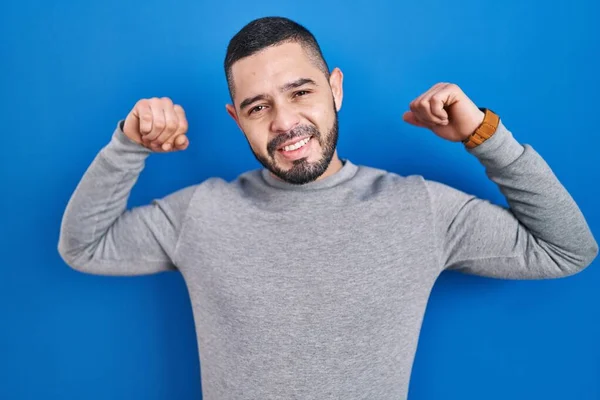 青い背景の上に立つヒスパニック系の男性は腕の筋肉を誇りに笑顔 フィットネスのコンセプト — ストック写真