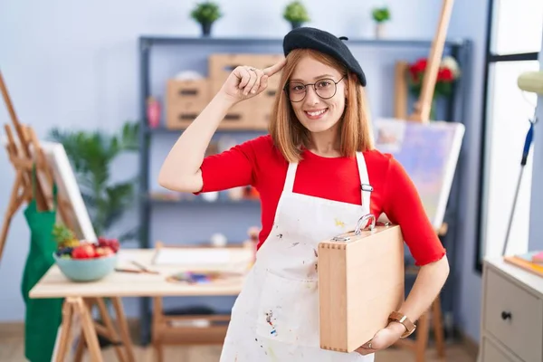 Young Redhead Woman Art Studio Holding Art Case Smiling Pointing — Stock Photo, Image