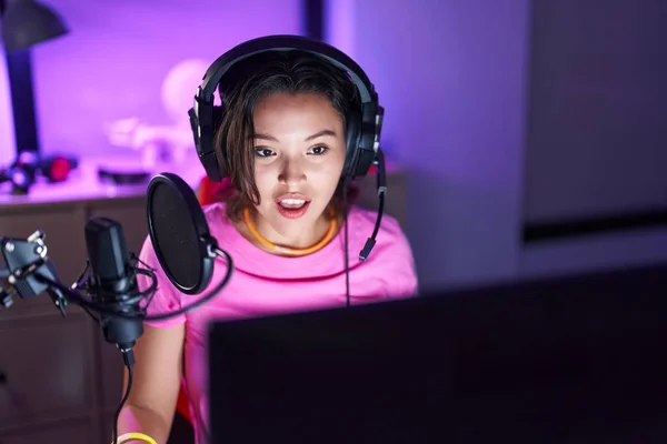 ヒスパニック系の若い女性がビデオゲームをプレイしている恐怖と驚きのために口を開けて驚いて 不信の顔 — ストック写真