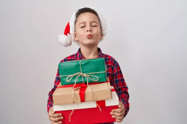 小男孩头戴圣诞礼帽 手里拿着礼物 看着摄像机 飞吻着一个可爱而性感的吻 爱的表达 — 图库照片